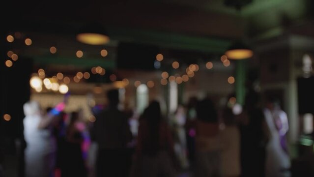 Defocused view of great wedding party with silhouettes of people dancing on the dancefloor. Slow motion.