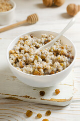 Kutya, a traditional Ukrainian Christmas dish made of wheat groats on the table for Christmas or the old New Year. Boiled porridge with walnuts, raisins, poppy seeds and honey in a white bowl.