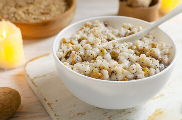 Kutya, a traditional Ukrainian Christmas dish made of wheat groats on the table for Christmas or the old New Year. Boiled porridge with walnuts, raisins, poppy seeds and honey in a white bowl.