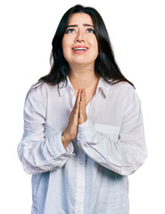 Beautiful hispanic woman wearing casual white shirt begging and praying with hands together with...