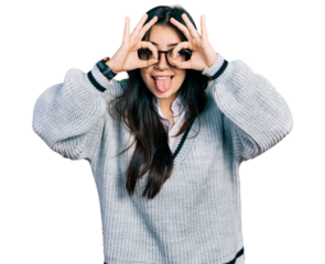 Beautiful hispanic woman wearing casual sweater and glasses doing ok gesture like binoculars sticking tongue out, eyes looking through fingers. crazy expression.