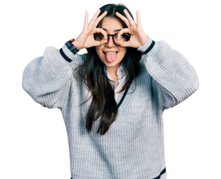 Beautiful hispanic woman wearing casual sweater and glasses doing ok gesture like binoculars sticking tongue out, eyes looking through fingers. crazy expression.