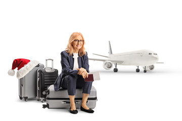 Middle aged woman sitting on a suitcase with a passport and ticket and waiting for a christmas flight