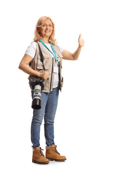Full length shot of a female photographer with a camera on shoulder strap gesturing thumbs up