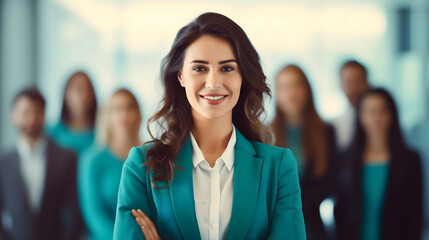 Fototapeta premium A beautiful young female entrepreneur in an elegant suit standing in a modern office interior, looking at the camera and smiling. A group of clients and coworkers in the background. Businesswoman