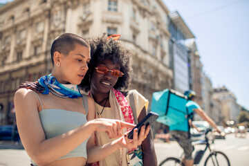 Two diverse young women in city using smartphone