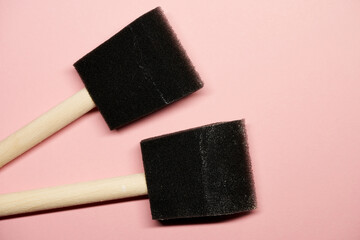 Two black foam paintbrushes on pink surface