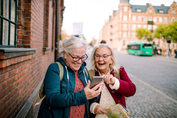 Two happy senior women checking smartphone on vacation in city