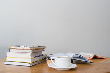 Cup of hot coffee drink, opened book and stack of books on wooden table, focus on foreground