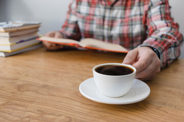 Unrecognizable man reading book and holding cup of coffee, studying or working, sitting at the...