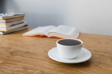 Cup of hot coffee drink, opened book and stack of books on wooden table, focus on foreground