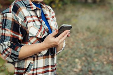 Woman in autumn plaid shirt holding smartphone in hands close-up