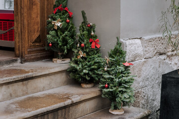 Christmas trees decorated with garlands, toys, and colorful balls stand on the steps of a house on the street. Photography, Christmas concept, New Year holiday.