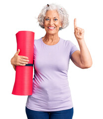 Senior grey-haired woman holding yoga mat surprised with an idea or question pointing finger with...