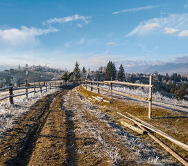 Winter coming. Last days of autumn, morning in mountain countryside peaceful picturesque hoarfrosted scene. Dirty road from hills to the village. Ukraine, Carpathian mountains.