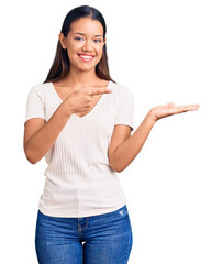 Fototapeta na wymiar Young beautiful latin girl wearing casual white t shirt amazed and smiling to the camera while presenting with hand and pointing with finger.