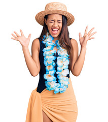 Young beautiful latin girl wearing hawaiian lei and summer hat celebrating mad and crazy for...