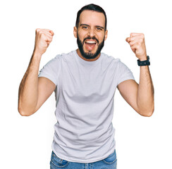 Young man with beard wearing casual white t shirt angry and mad raising fists frustrated and furious while shouting with anger. rage and aggressive concept.