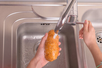 Female hands washing potato with hand under running water in sink in the kitchen. Vegetables,...