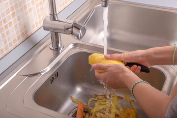 Female hands washing a peeling potato with hand under running water in sink in the...