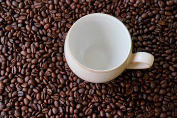 Empty coffee mug on coffee beans background with dramatic light and copy space