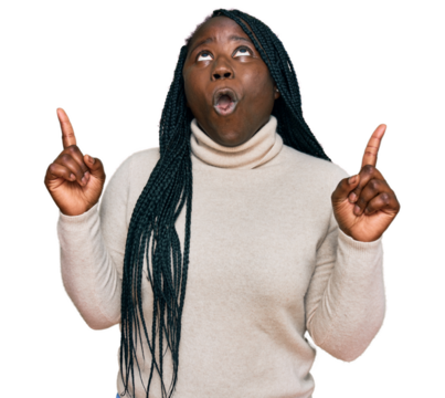 Young black woman with braids wearing casual winter sweater amazed and surprised looking up and pointing with fingers and raised arms.