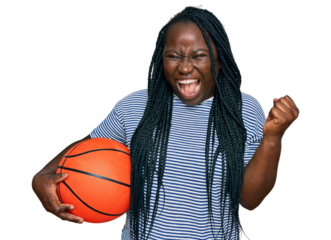 Young black woman with braids holding basketball ball screaming proud, celebrating victory and success very excited with raised arms