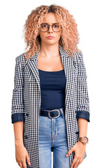 Young blonde woman with curly hair wearing business jacket and glasses skeptic and nervous,...