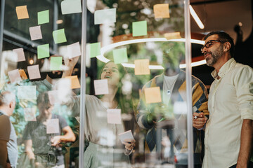 Diverse business group brainstorming and collaborating in a glass-walled office. Sharing ideas with...