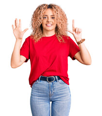 Young blonde woman with curly hair wearing casual red tshirt showing and pointing up with fingers number seven while smiling confident and happy.