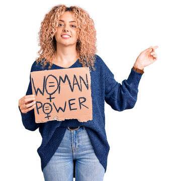 Young blonde woman with curly hair holding we need a change banner smiling happy pointing with hand and finger to the side
