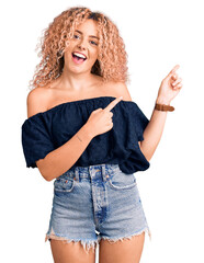 Young blonde woman with curly hair wearing casual summer clothes smiling and looking at the camera pointing with two hands and fingers to the side.