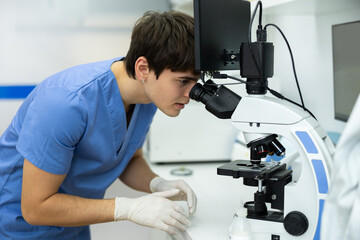 Concentrated young veterinarian using digital microscope to examine blood or skin samples of animal...