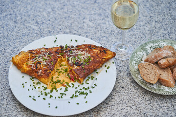 Close up picture on simple french style egg omelette with cheese and choped fresh chives served with slices of whole grain baguette and glass of white wine as a small and quick lunch in french bistro.