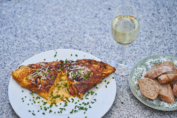 Close up picture on creamy egg omelette with sheep cheese and sprinkled by fresh green chives with slices of rustic whole grain baguette and glass of dry white wine. Quick and light dish from Bistro.