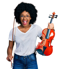 Young african american woman playing violin celebrating crazy and amazed for success with open eyes...