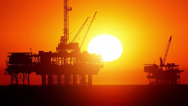 Sun setting behind two offshore oil platform off the coast of California