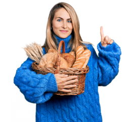 Young blonde woman holding wicker basket with bread smiling with an idea or question pointing finger with happy face, number one