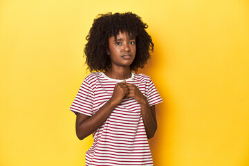 Teen girl in red striped T-shirt, yellow studio backdrop scared and afraid.