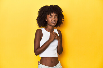 Teen girl in white tank top, yellow studio background scared and afraid.