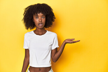 Teen girl in classic white T-shirt, yellow studio backdrop impressed holding copy space on palm.