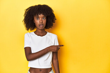 Teen girl in classic white T-shirt, yellow studio backdrop pointing to the side