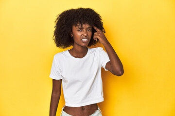 Teen girl in classic white T-shirt, yellow studio backdrop showing a disappointment gesture with forefinger.