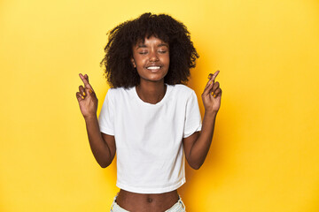 Teen girl in classic white T-shirt, yellow studio backdrop crossing fingers for having luck
