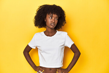 Teen girl in classic white T-shirt, yellow studio backdrop confused, feels doubtful and unsure.