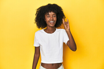 Teen girl in classic white T-shirt, yellow studio backdrop showing a horns gesture as a revolution concept.
