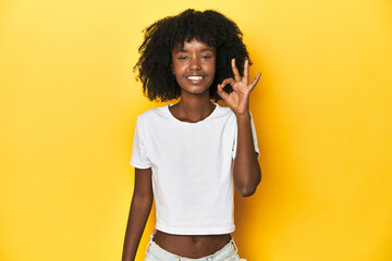 Teen girl in classic white T-shirt, yellow studio backdrop cheerful and confident showing ok...