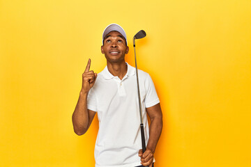 African American man golfer, yellow studio backdrop, pointing upside with opened mouth.