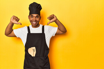 African American cook with utensils, yellow studio, feels proud and self confident, example to...