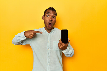 African American man with mobile phone, yellow studio, pointing to the side